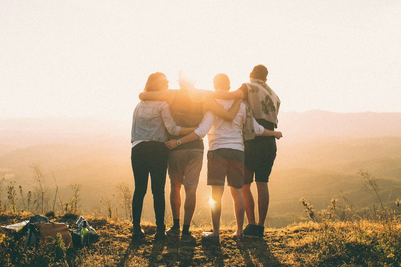 Four people arm in arm looking out over a valley at sunset