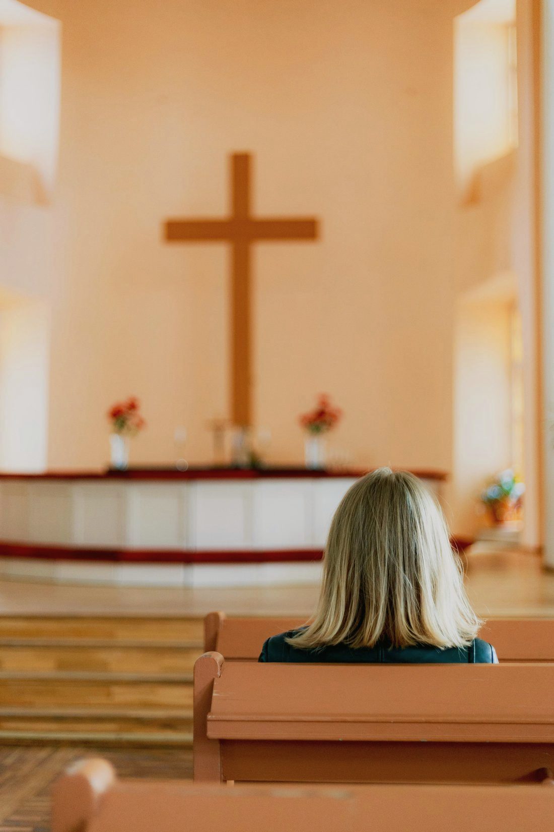 A woman sitting alone in a sunlit sanctuary, facing the cross